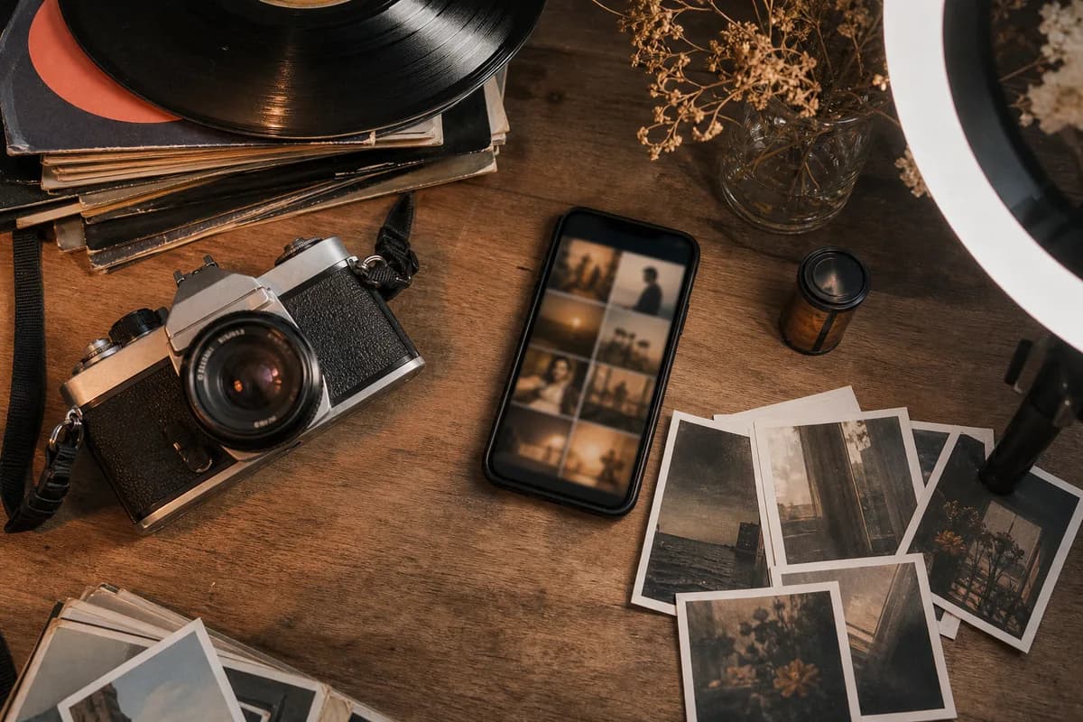 Young person's desk with a film camera, vinyl records, a ring light and a smartphone showing a blurred vintage-styled feed.
