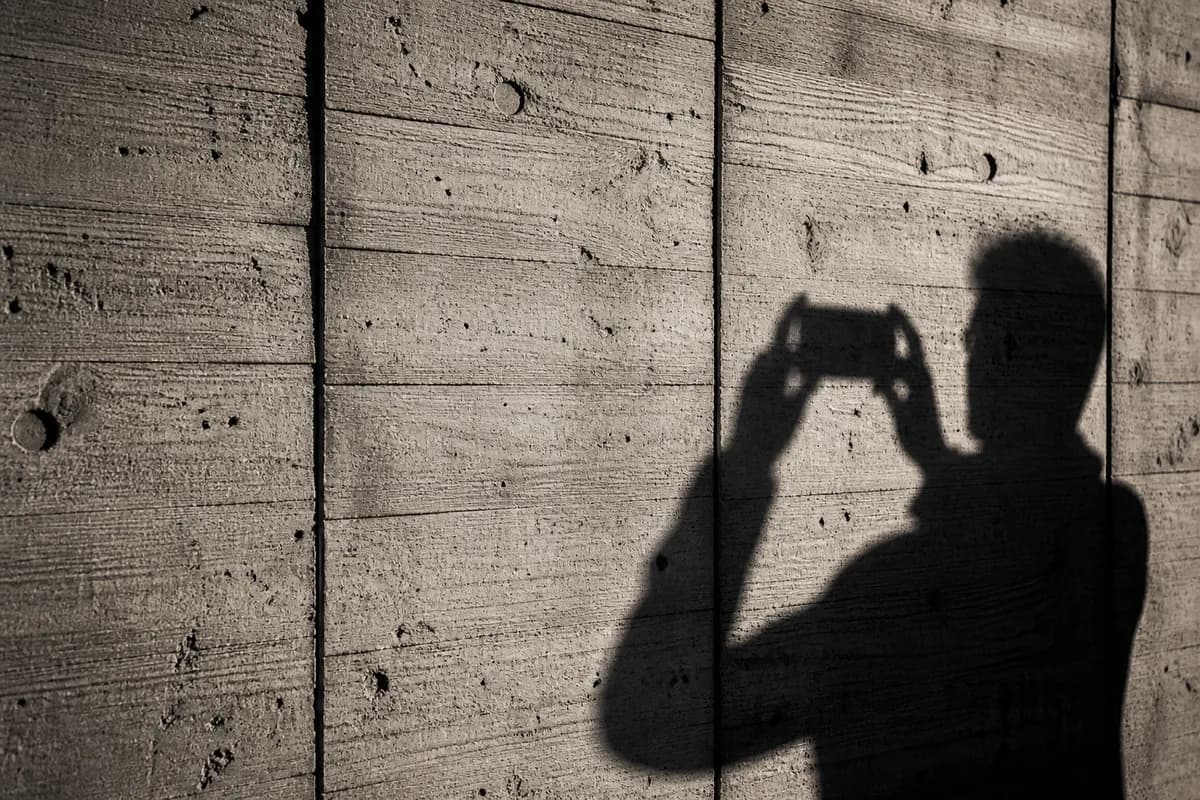 Close view of raw board-marked concrete with strong afternoon light, phone photographer's shadow falling on the wall
