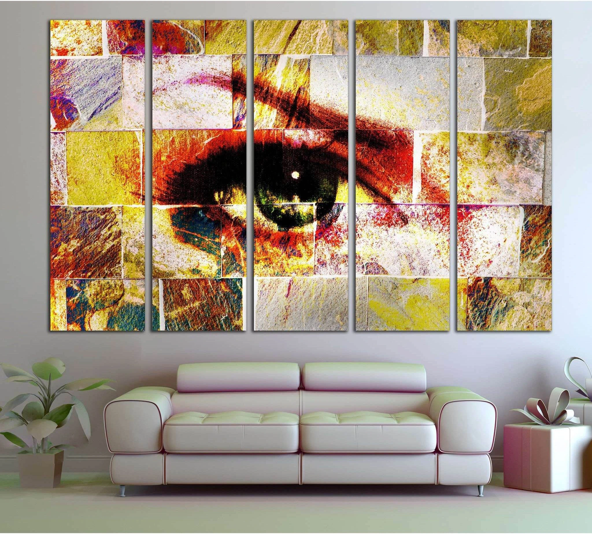 Abstract eye canvas print in yellow gold and red mosaic texture, displayed above a sofa in a modern living room