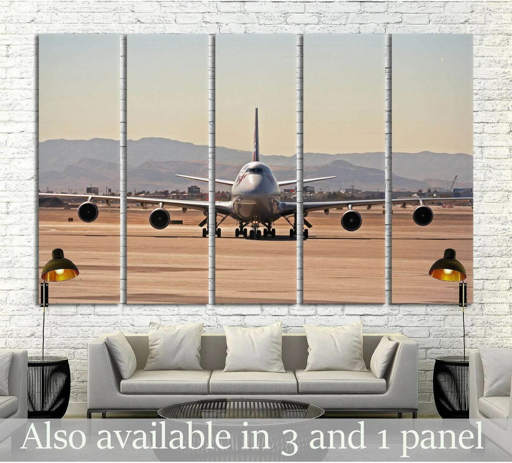 Front-facing jumbo jet canvas print on runway with distant mountains, shown above sofa in modern living room