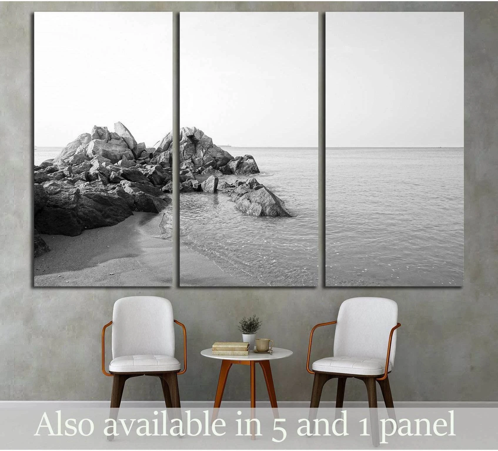 Black and white seascape canvas print with rocky shoreline hung above chairs in a minimalist living room