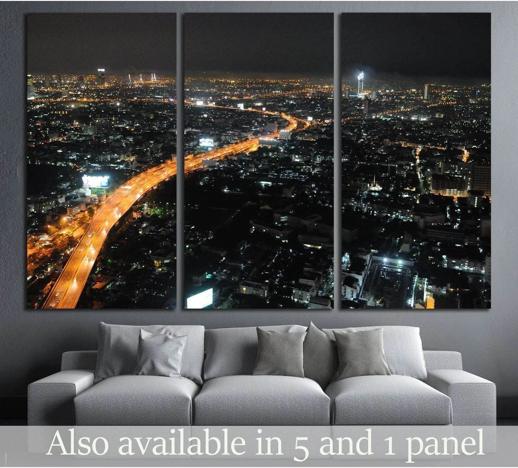 Triptych night cityscape canvas print with glowing highway lights above a gray sofa