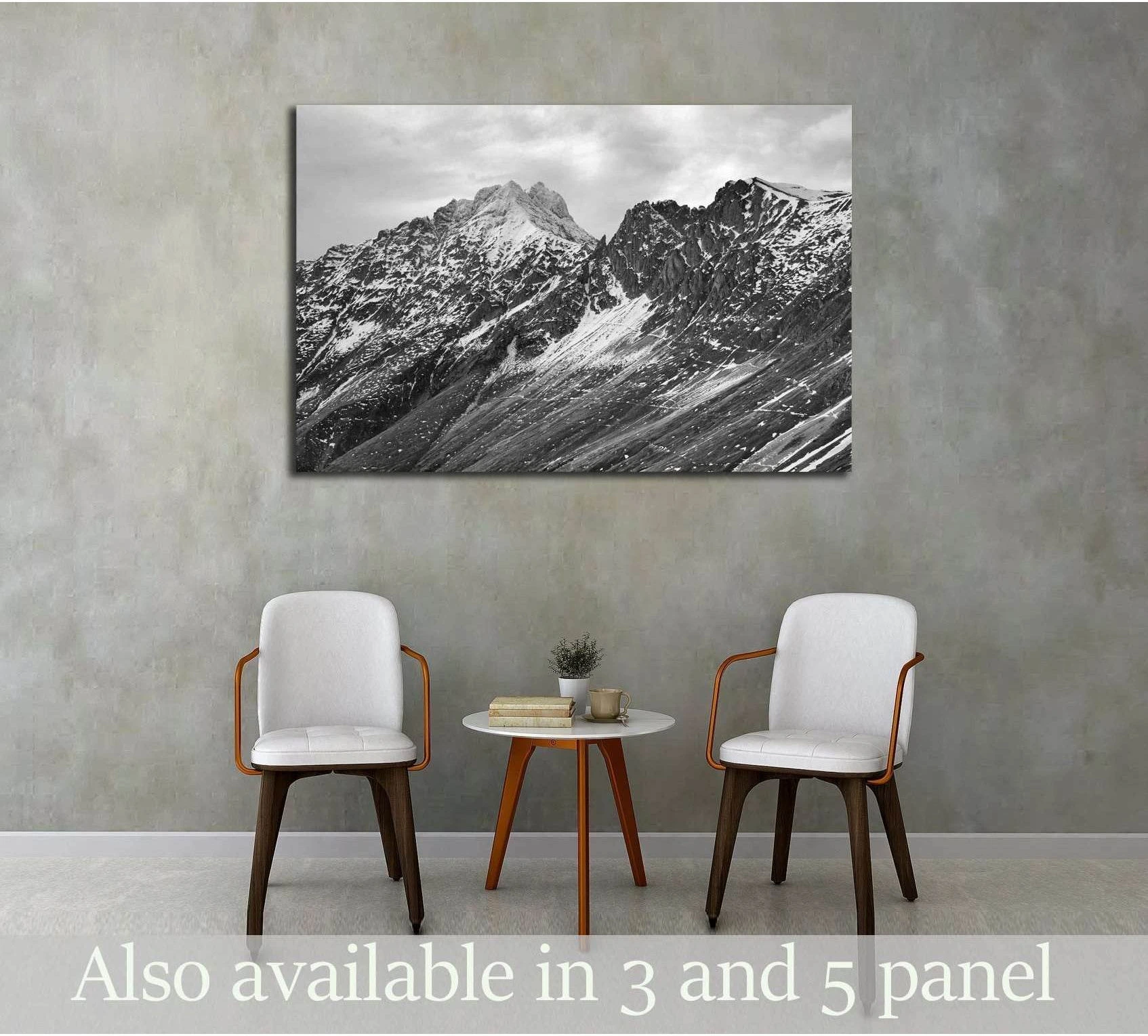 Black and white mountain canvas print with snowy alpine peaks hung above chairs in a minimalist room