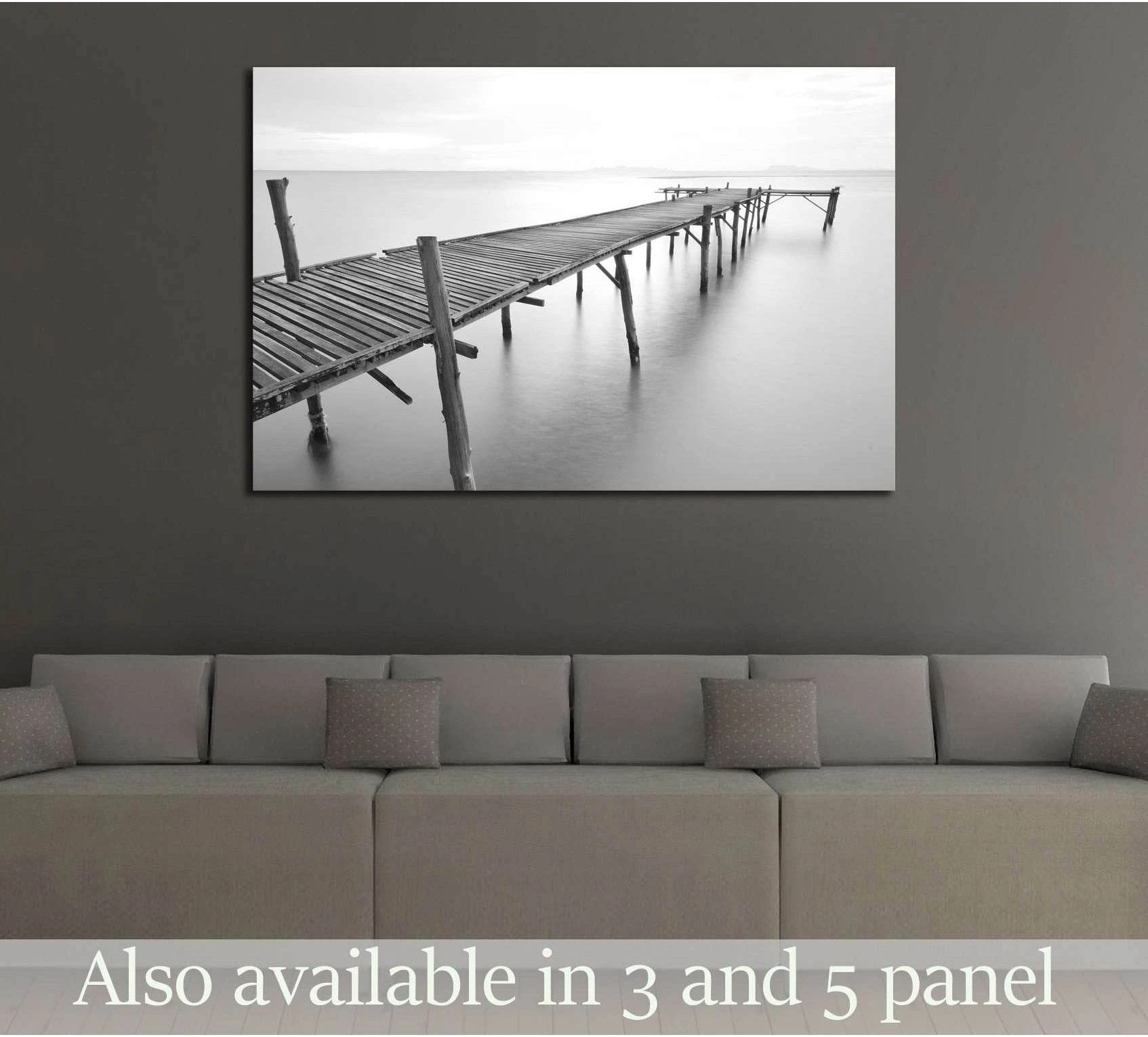 Black and white pier canvas print above sofa in modern living room with calm sea horizon