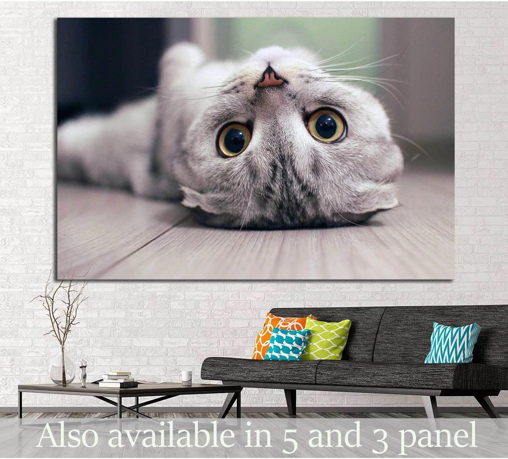 Upside-down grey cat canvas print with big yellow eyes displayed above a sofa in a modern living room