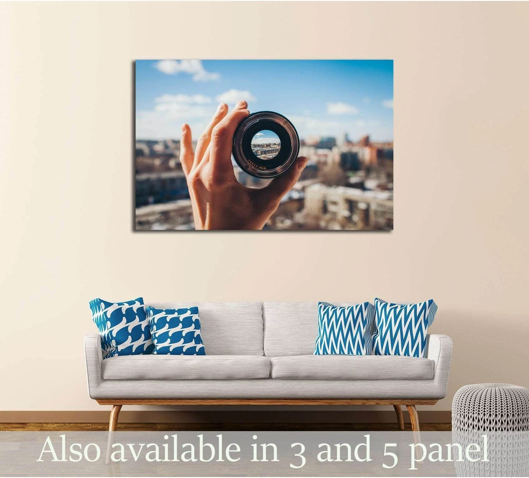 Hand holding a camera lens framing a blurred city skyline canvas print above a sofa