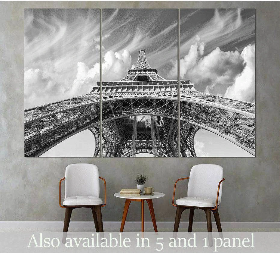 Black and white Eiffel Tower triptych canvas print above chairs in a modern living room