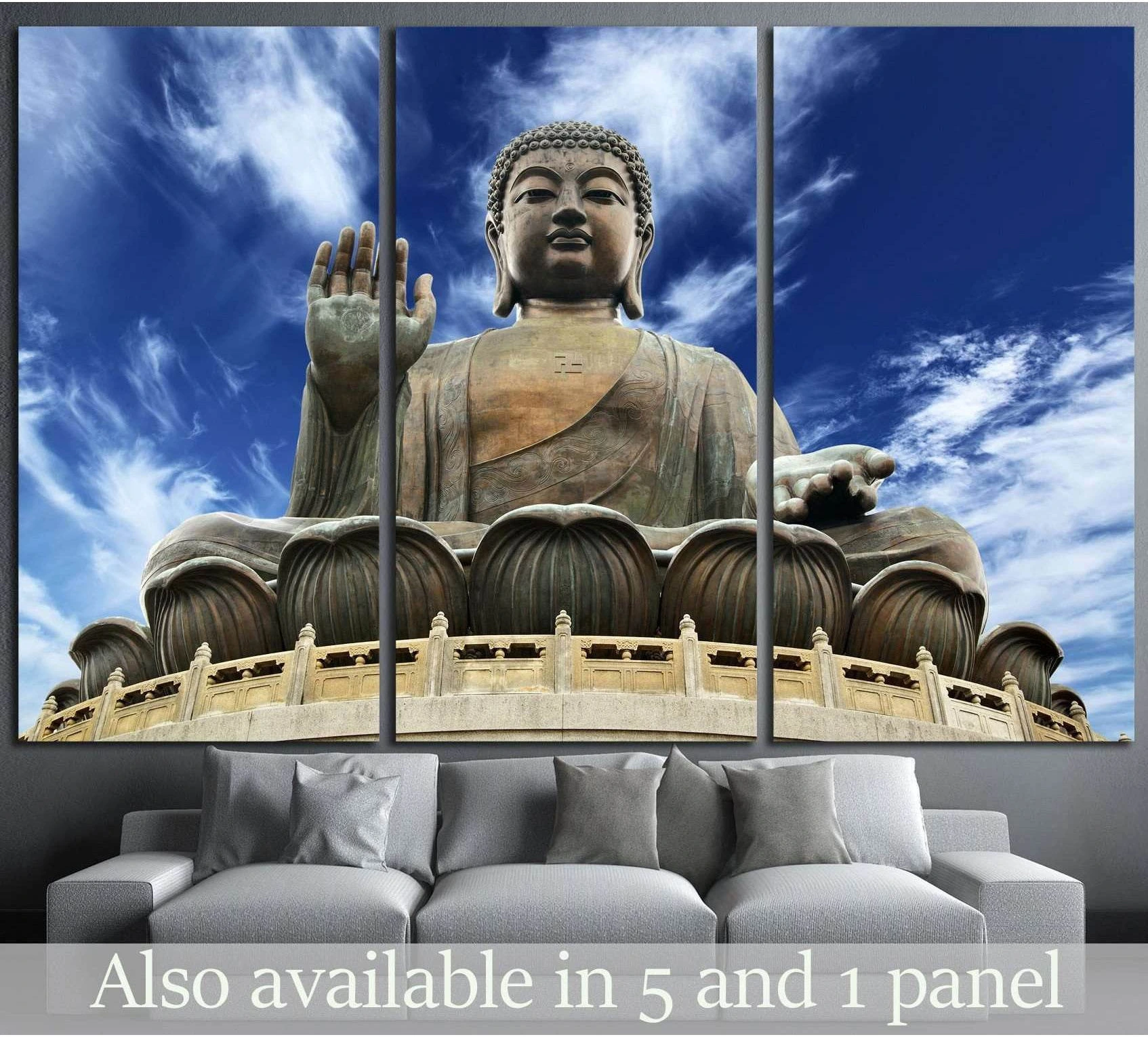Giant Buddha canvas print in bronze tones against a blue sky, displayed above a sofa in a modern living room
