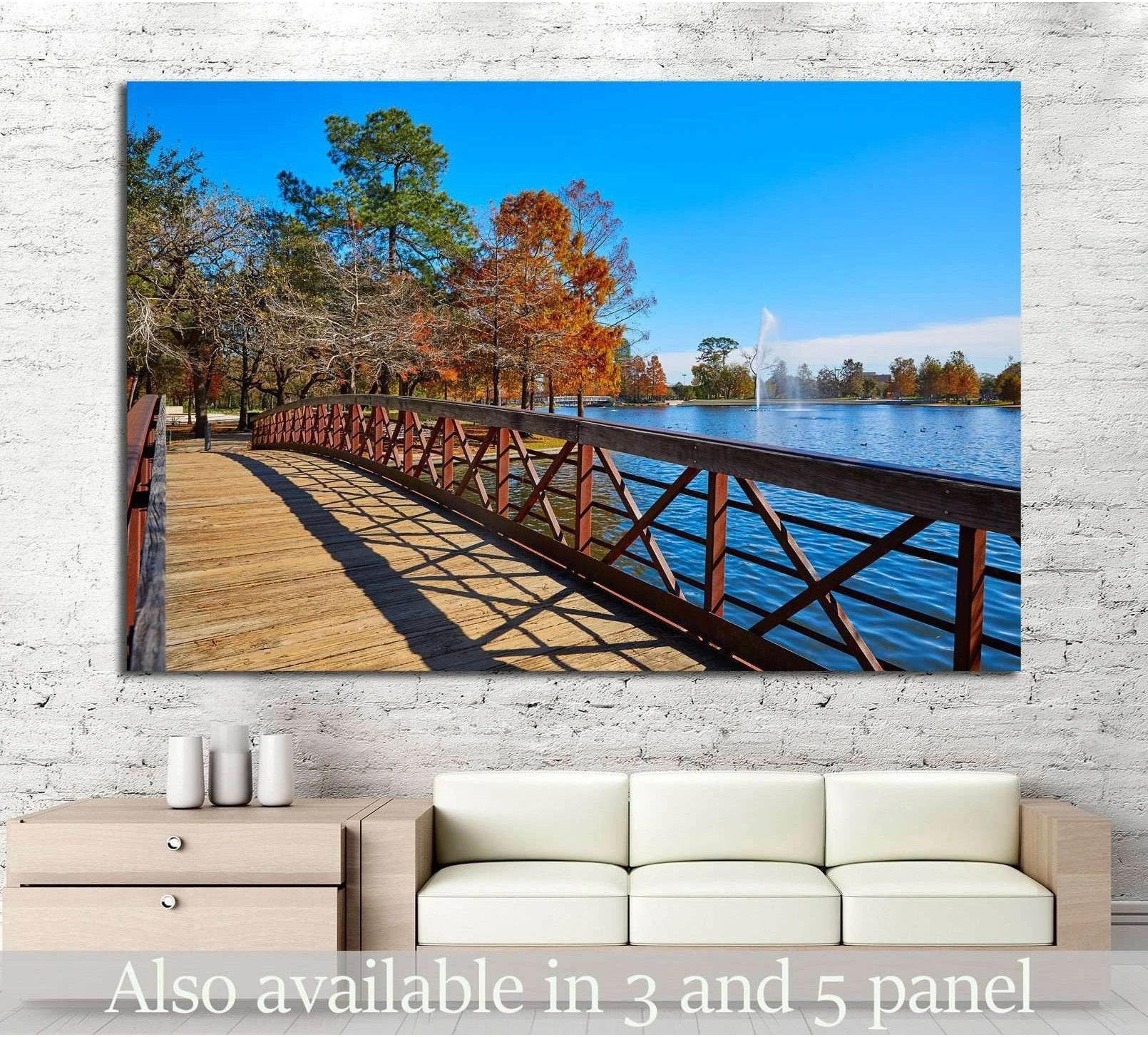 Hermann Park canvas print with wooden lakeside bridge, autumn trees, and fountain above sofa