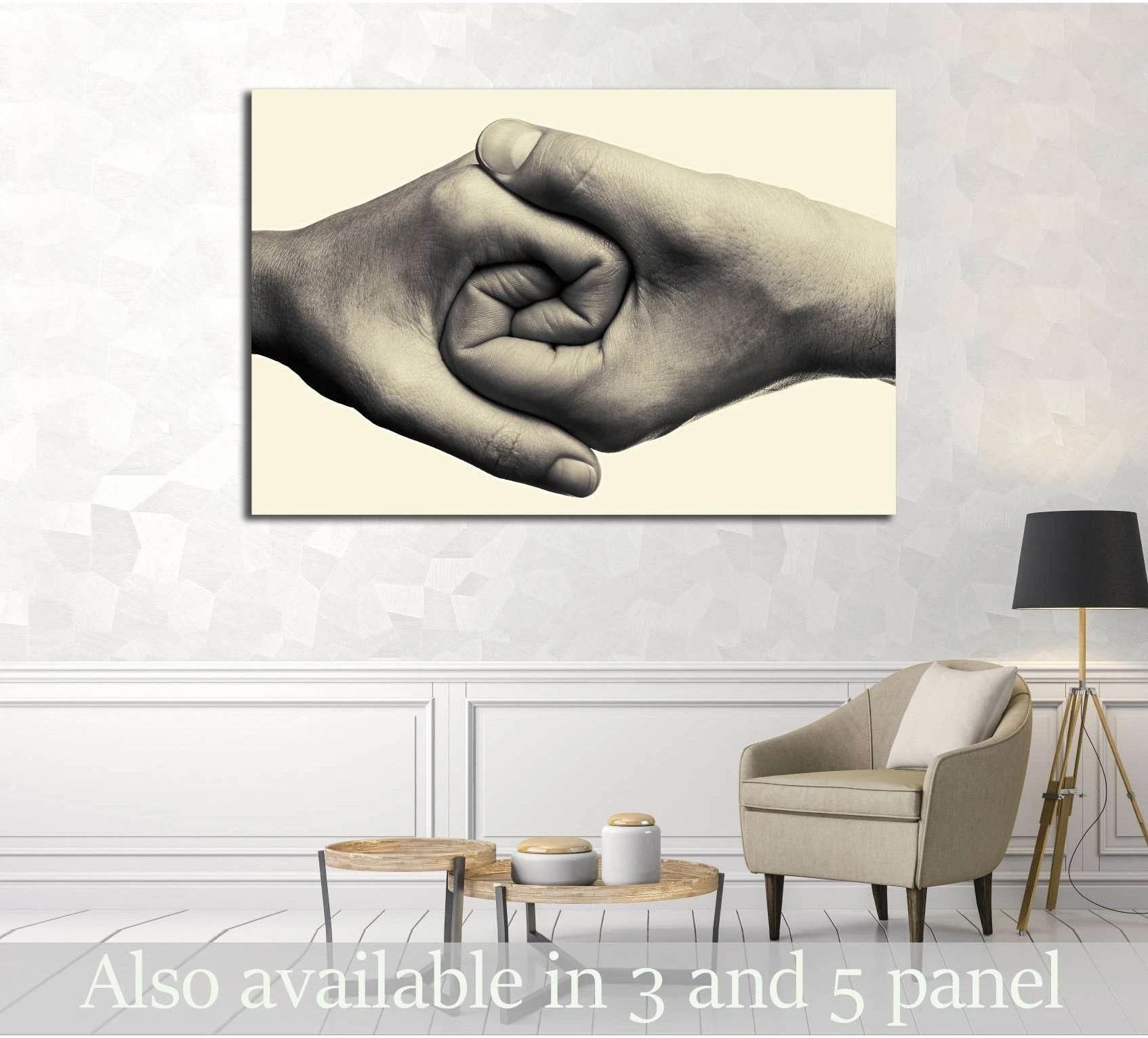 Black and white hands holding canvas print displayed above chair in a neutral living room