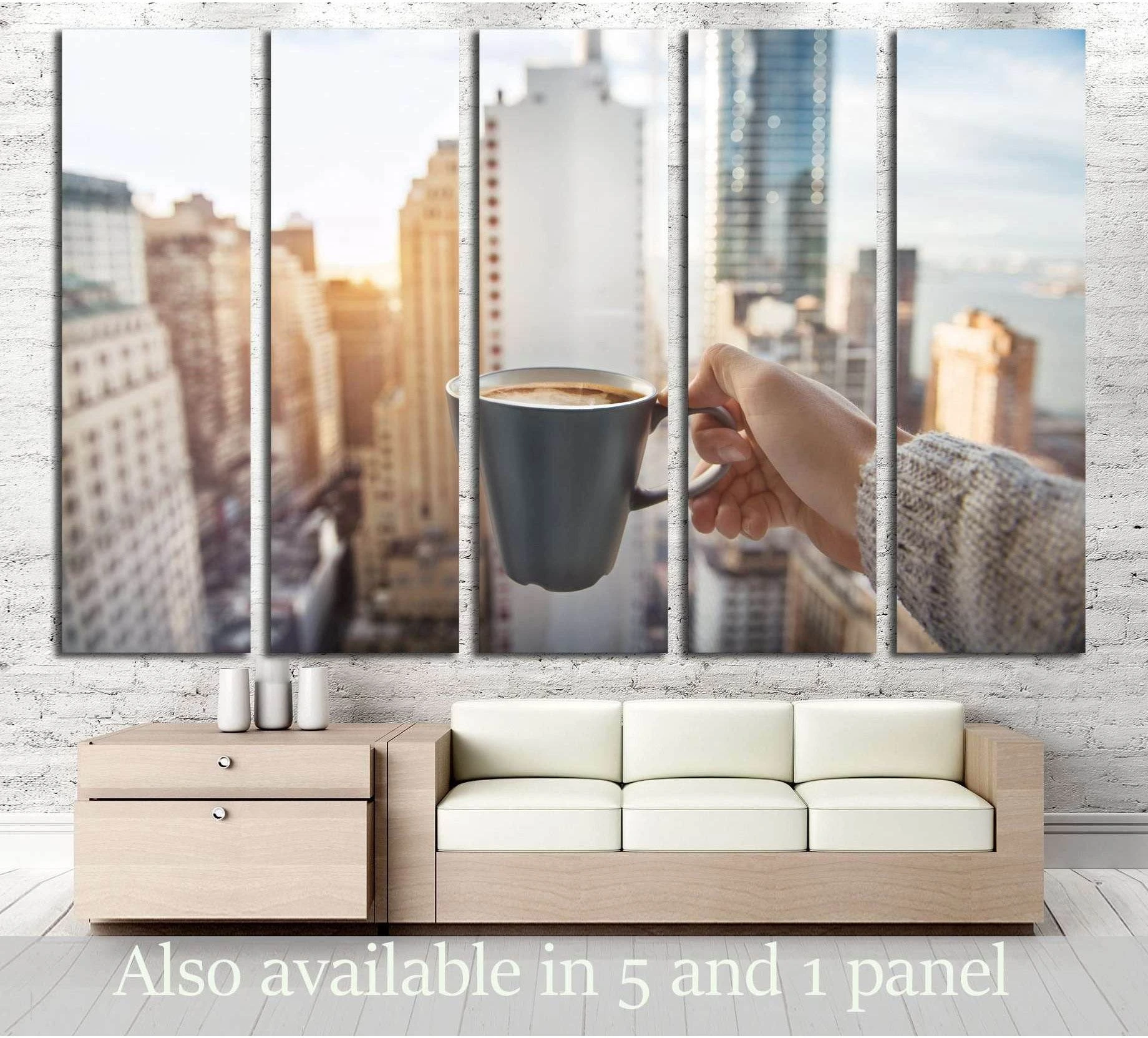 Hand holding coffee cup with blurred Manhattan skyline canvas print above sofa in modern living room