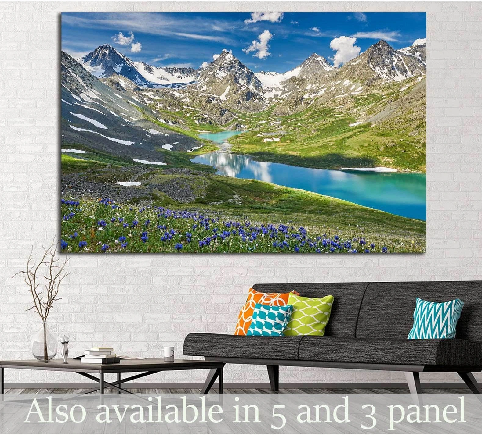 Panoramic mountain lake canvas print with turquoise alpine water, snowy peaks, and wildflowers above a sofa