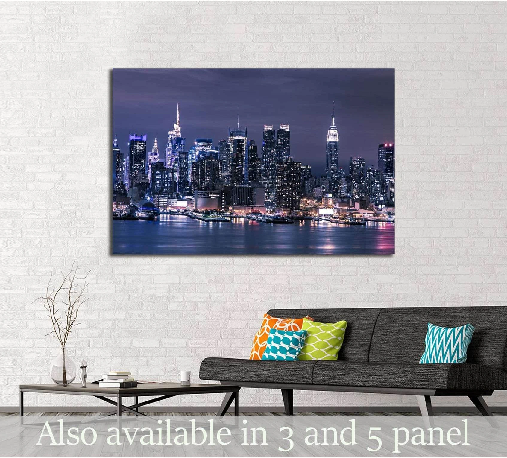 Manhattan skyline canvas print at night over the Hudson River, displayed above a sofa in a modern living room