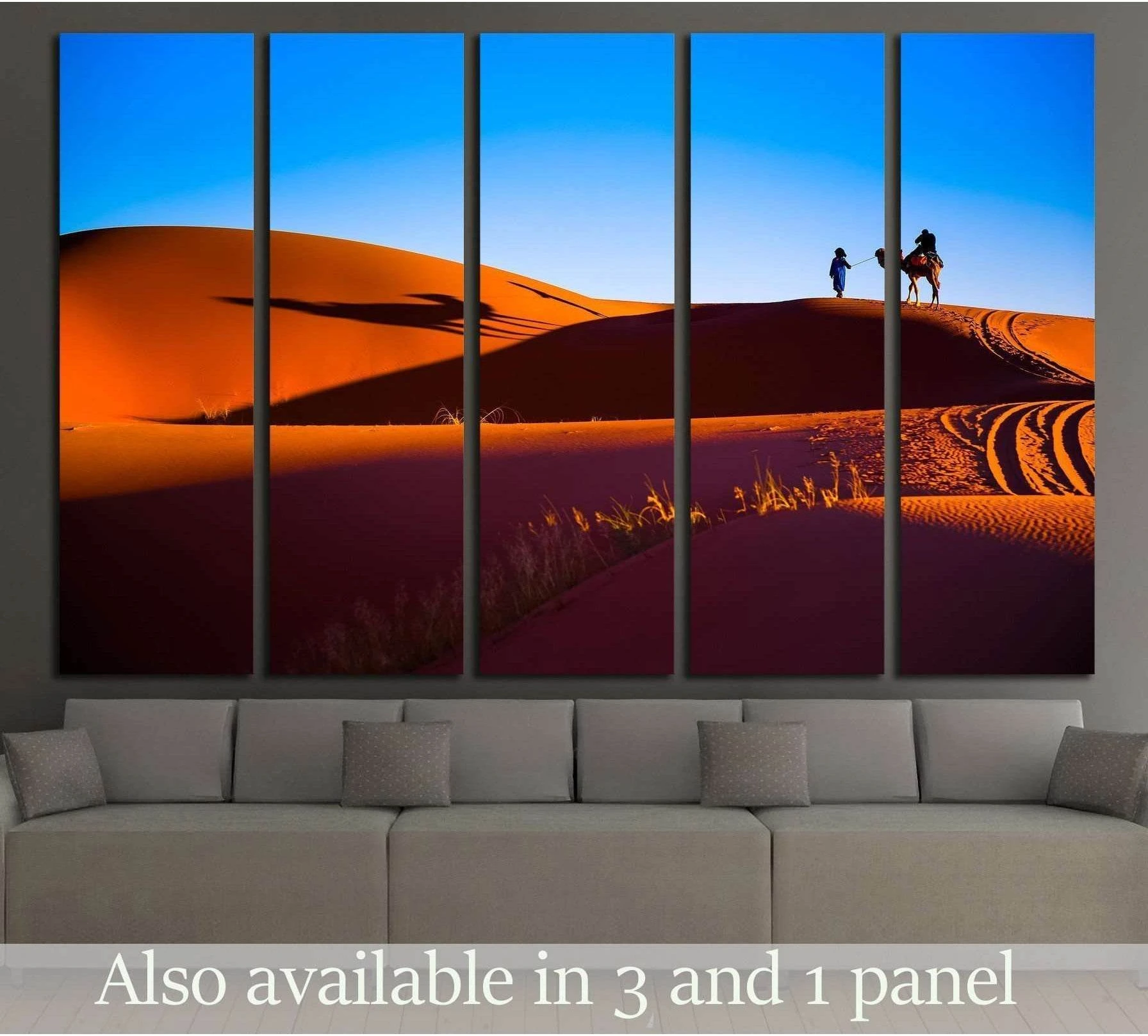 Sahara desert canvas print with orange sand dunes, camel silhouettes, and blue sky above a sofa