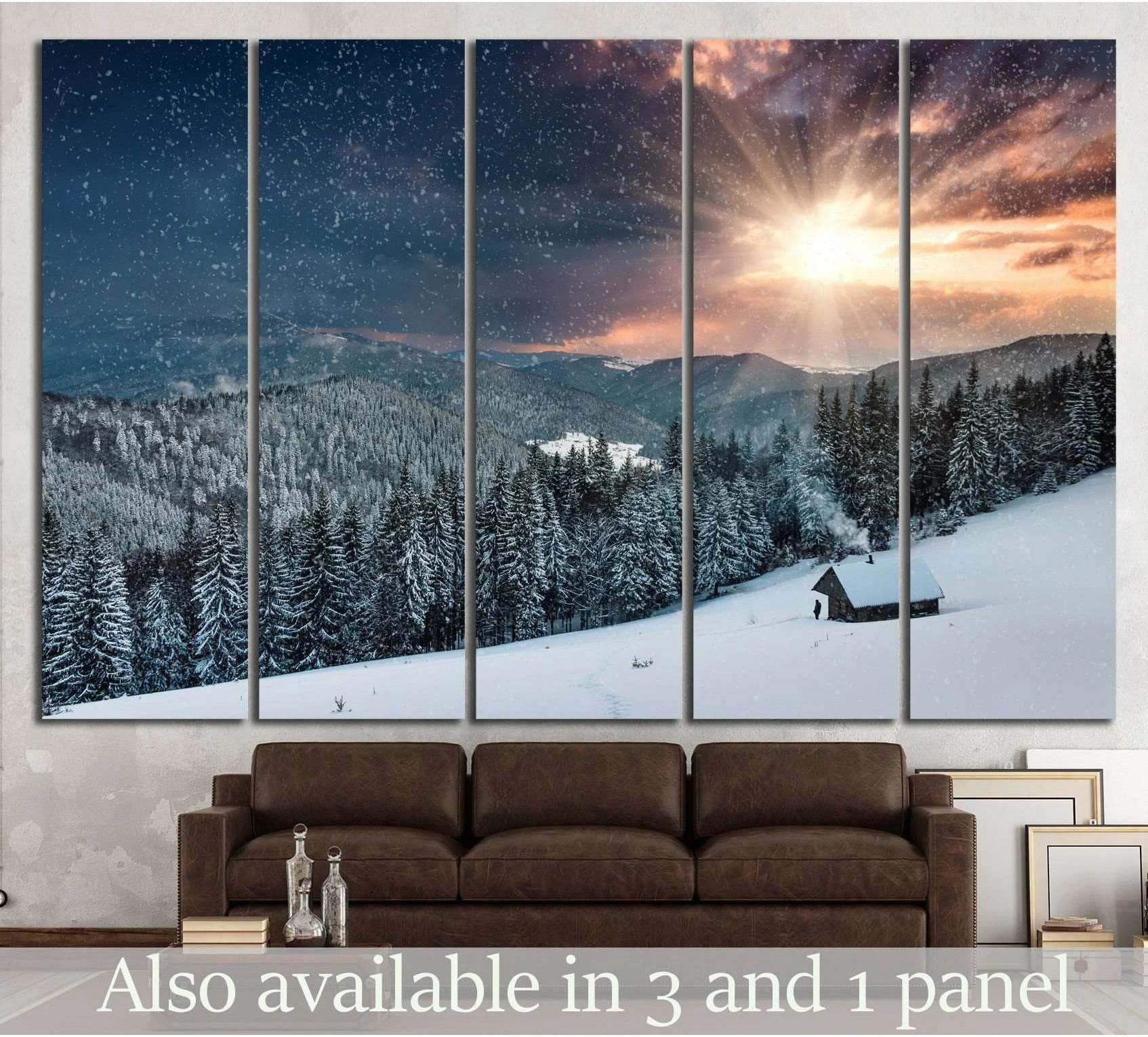 Snowy mountain cabin canvas print with glowing winter sunset over pine forest, hung above a brown sofa