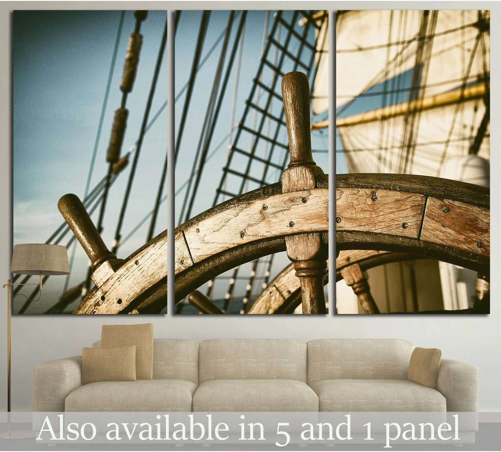 Weathered wooden ship wheel canvas print with sail rigging and sunlit sails above a sofa in a coastal living room